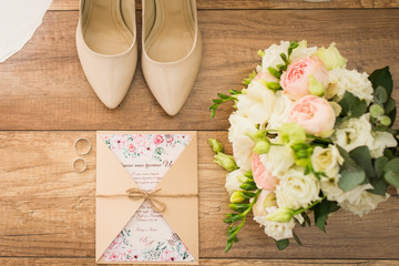 Wedding accessories: bridal shoes, rings, invitation, bouquet. Wedding details in beige shades. View from above