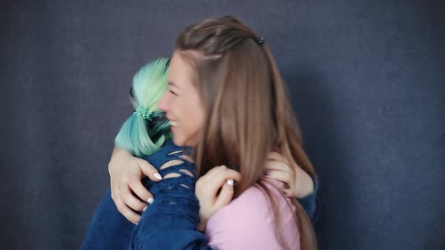 Two beautiful girl sharing secret information with shocked surprised telling interesting funny news on a gray background