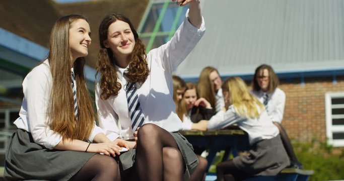 4K Happy female school friends posing for selfie & laughing outside school building. Slow motion