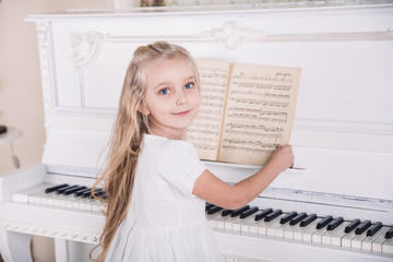 little blond girl play on white piano in white dress © phpetrunina14