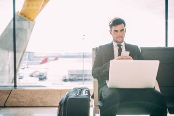Young business man sitting on the computer and mobile phone with the suitcase at the airport...