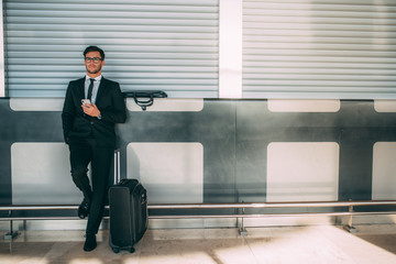 Young business man standing on the phone with the suitcase at the airport waiting for the flight ..