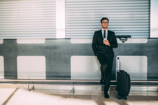 Young business man standing on the phone with the suitcase at the airport waiting for the flight ..