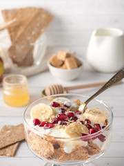 Glass bowl with muesli and yogurt with banana, pomegranate seeds