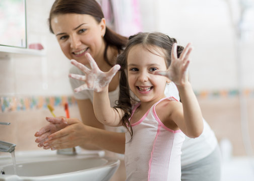child girl and mother washing hands with soap in bathroom