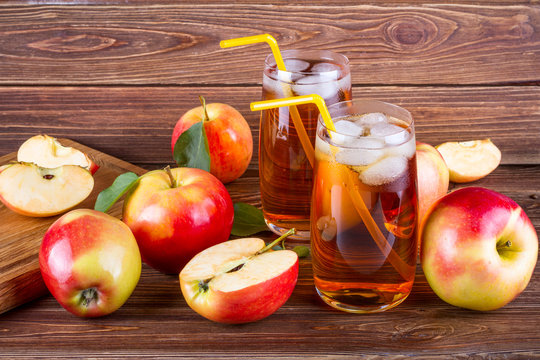 Fresh organic farm apple juice with ice in glass with raw whole and sliced red apples on woody background