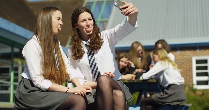 4K Happy schoolgirl friends pulling faces & posing for selfie outdoors at break time. Slow motion