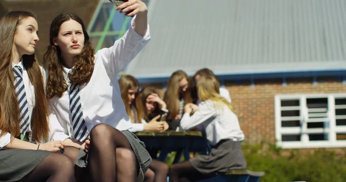 4K Teen girl friends at school pulling duck face pout to take a selfie outdoors at break time. Slow motion