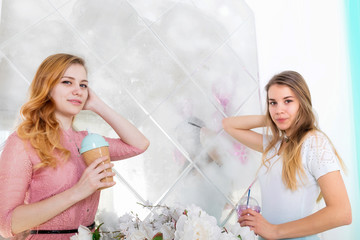 Two cute girls in dresses drink drinks from cups with lids and tubes