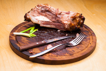 Pork bone with knife and fork, leftovers on a table after big dinner