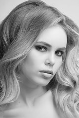 Naklejka premium Portrait of blonde girl with makeup and hairstyle from curly hair on grey background close-up black and white image.