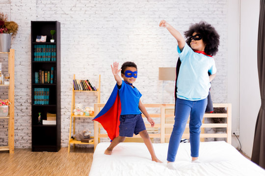African American happy and confident young kids playing and dressing up as superhero together in bedroom.
