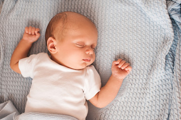 Sleeping baby lying in bed on knitted blanket closeup. Top view.