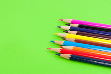Row of colorful wooden pencils on background of green paper