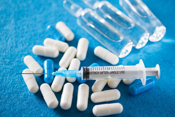 White and blue pills, syringe and ampoules on a blue background.