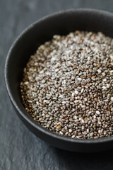 Chia seeds in a black metal bowl on a black textured board. Macro photography.
