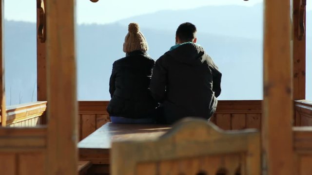 couple sitting wooden pavilion back view hugging enjoying amazing mountains horizon winter nature landscape man embracing woman romantic date honeymoon trip vacation recreation resort leisure