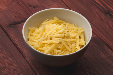 Grated cheese in white bowl on wooden table