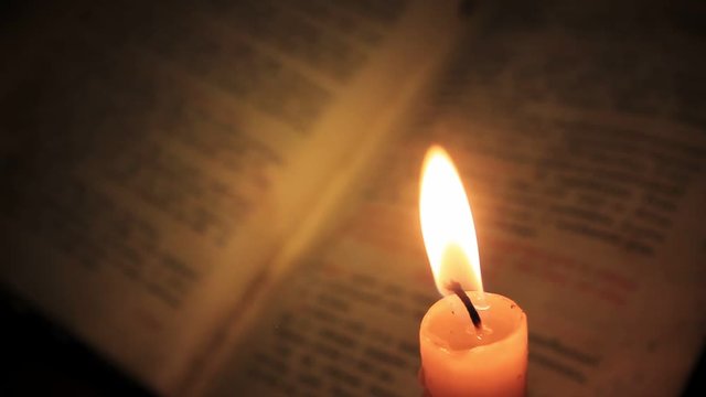 The vibrating flame of the candle above the old book with the text written by the Cyrillic. Refocusing from the candle to the book and back.