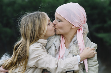 A woman with cancer is  next to her daughter. A girl is hugging a woman happy