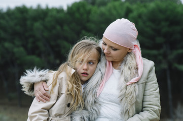 A woman with cancer is  next to her daughter. A girl is hugging a woman happy