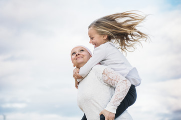 A woman with cancer is  next to her daughter. A girl is hugging a woman happy