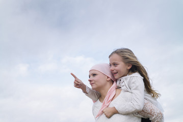 A woman with cancer is  next to her daughter. A girl is hugging a woman happy