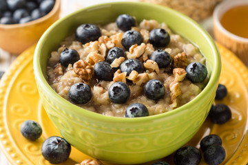 Oatmeal porridge with blueberries, walnuts and honey on white wooden background.