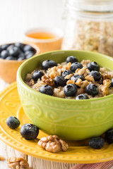 Oatmeal porridge with blueberries, walnuts and honey on white wooden background.