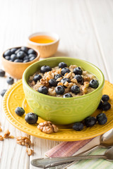 Oatmeal porridge with blueberries, walnuts and honey on white wooden background.