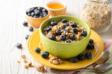 Oatmeal porridge with blueberries, walnuts and honey on white wooden background.