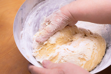 Women's hands knead the dough in a metal bowl with flour