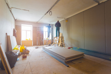 Workers are installing plasterboard (drywall) for gypsum walls in apartment is under construction,...
