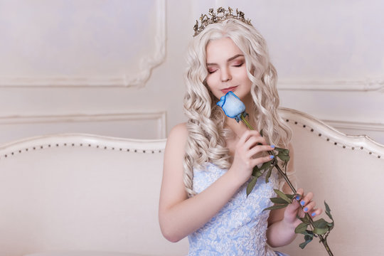A glamorous girl, a blond woman in a crown holds a blue rose and sniffs it. Aroma of flowers, Cinderella, Princess in the castle. A rich queen in a dress. Place your text here.