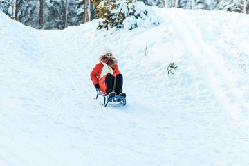 Fototapeta na wymiar A girl with sledge. Beautiful teenage girl in red down jacket having fun outside in a wood with snow in winter on a wonderful frosty sunny day. active life consept