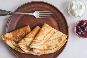 Pancakes with yoghurt and jam on a clay plate and rustic light background