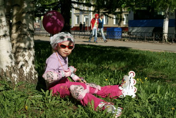 Little girl in roller blades sitting on the grass
