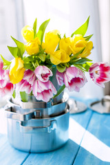 A bouquet of spring tulips of yellow and pink in new saucepans by the window. A gift to a woman. Cozy house. Card.