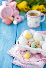 Breakfast in the spring morning. Yellow and pink tulips. A refrigerator. A coffee in a beautiful mug. Same eggs. Pascha. A dining room napkin. A blue wooden background. An opening and text.