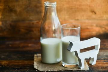 milk bottle, glass of milk, a figure of a cow the concept of a village power, farm-fresh products on a natural wooden background
