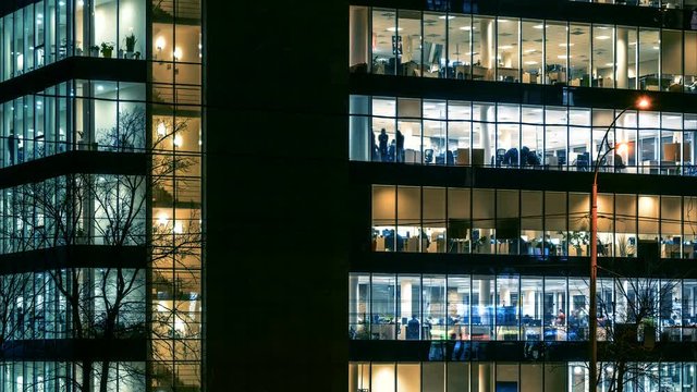 Skyscraper with glowing windows and a lot of people inside working overtime at night. Time lapse 