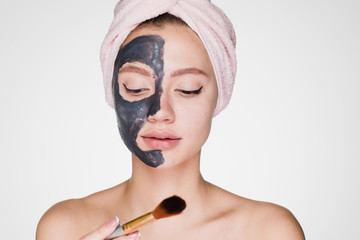 cute young girl with a pink towel on her head puts on face clay mask
