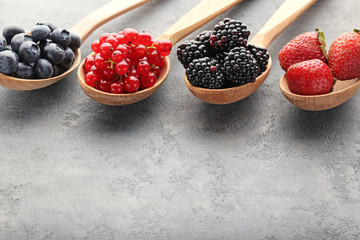 Ripe and sweet berries in spoons on grey wooden table