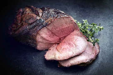 Barbecue dry aged haunch of venison with herbs as close-up on a board - obrazy, fototapety, plakaty
