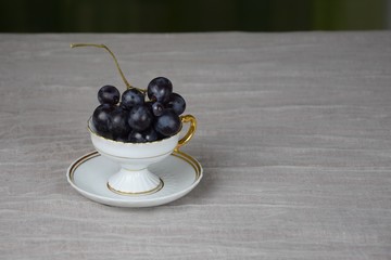 Blue grapes in the coffee cup, light background