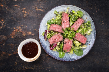 Barbecue wagyu point steak slices with mixed lettuce and hot sauce as top view on a plate
