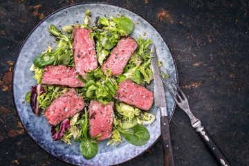 Barbecue wagyu point steak slices with mixed lettuce as top view on a plate