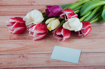 Beautiful tulip bouquet laying on light wooden background near white blank card