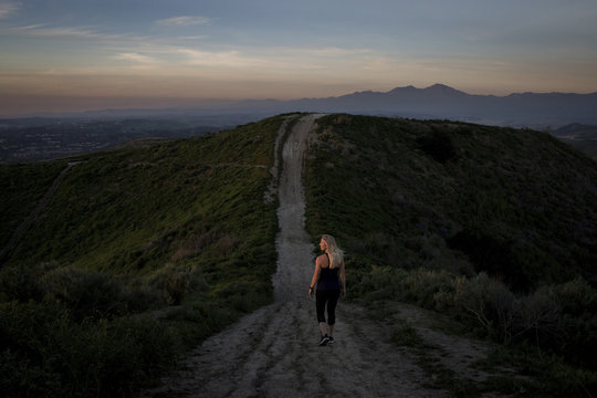 Rear View Of Woman Walking On Mountain Trail During Sunset