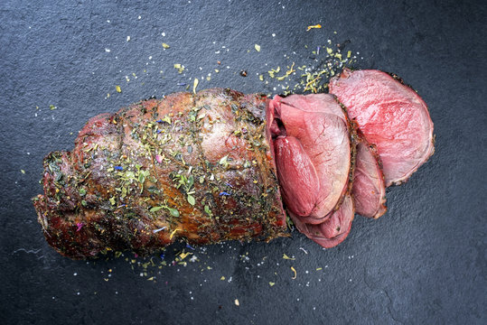 Barbecue dry aged haunch of venison with herbs as close-up on a black board